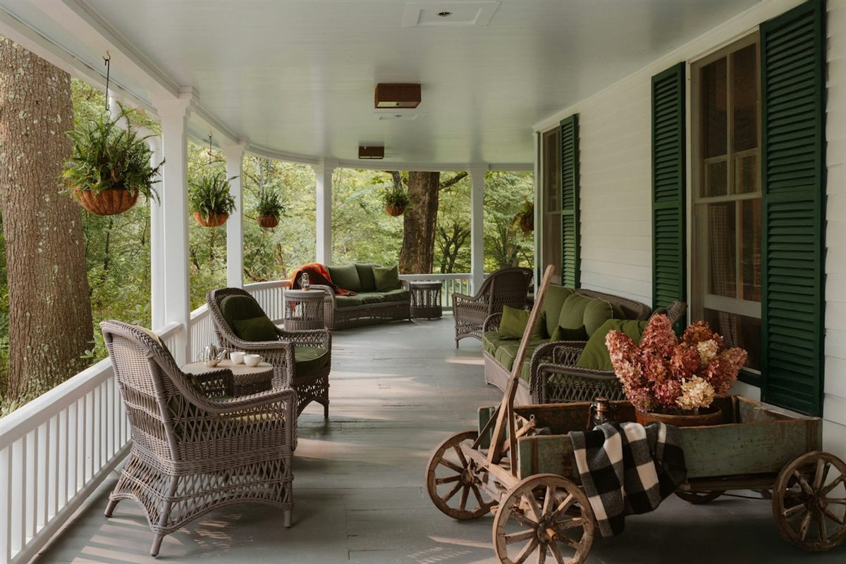 Wide covered farmhouse porch with wicker chairs and green shutters