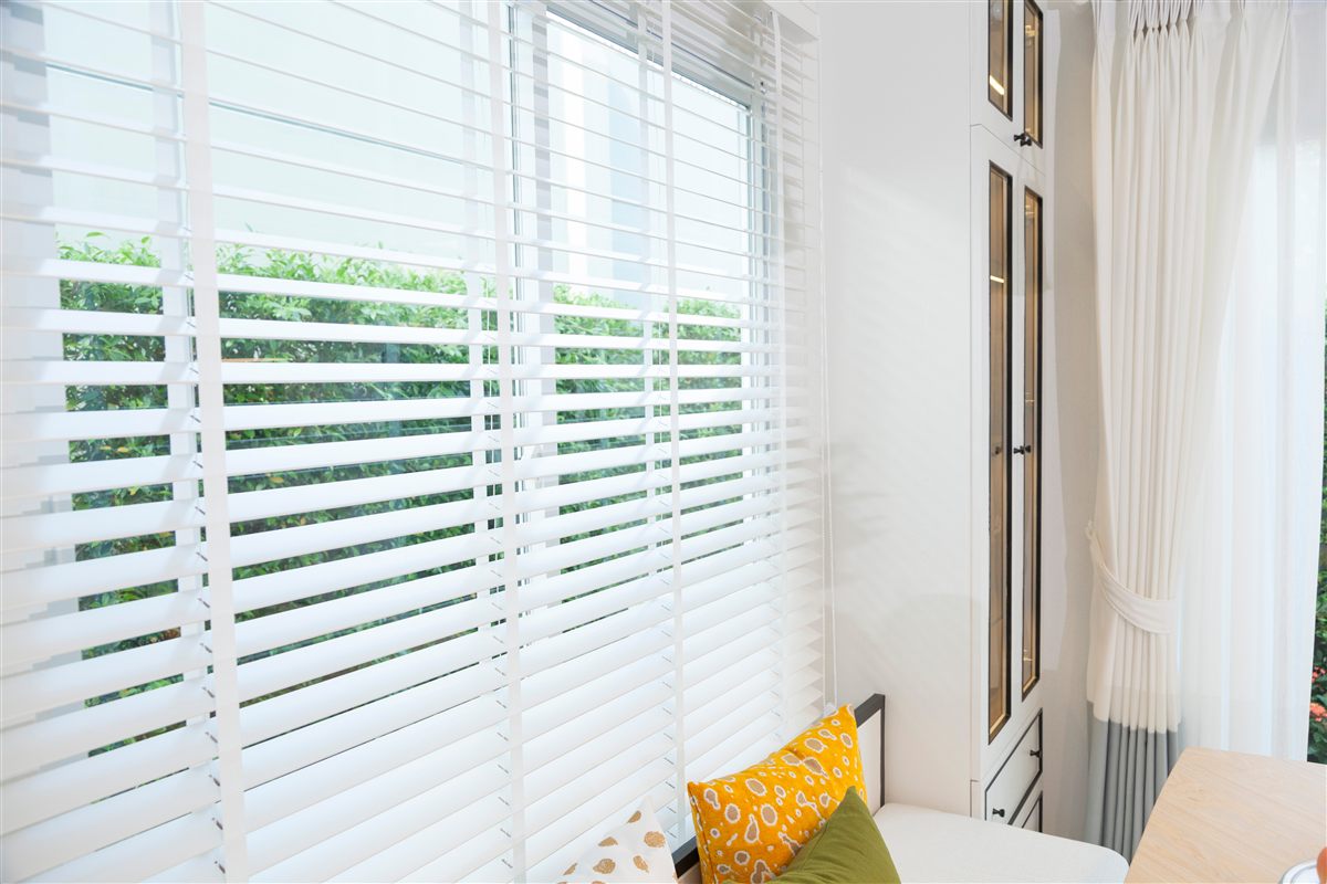 White wood blinds on a window above a cushioned window seat